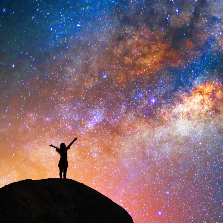Silhouette of a person on a mountain top with a vibrant starry sky