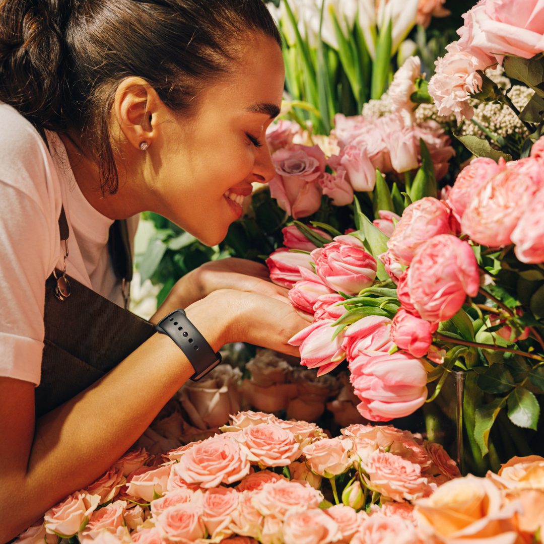 A woman inhales the fragrance of colorful flowers, surrounded by various floral arrangements.