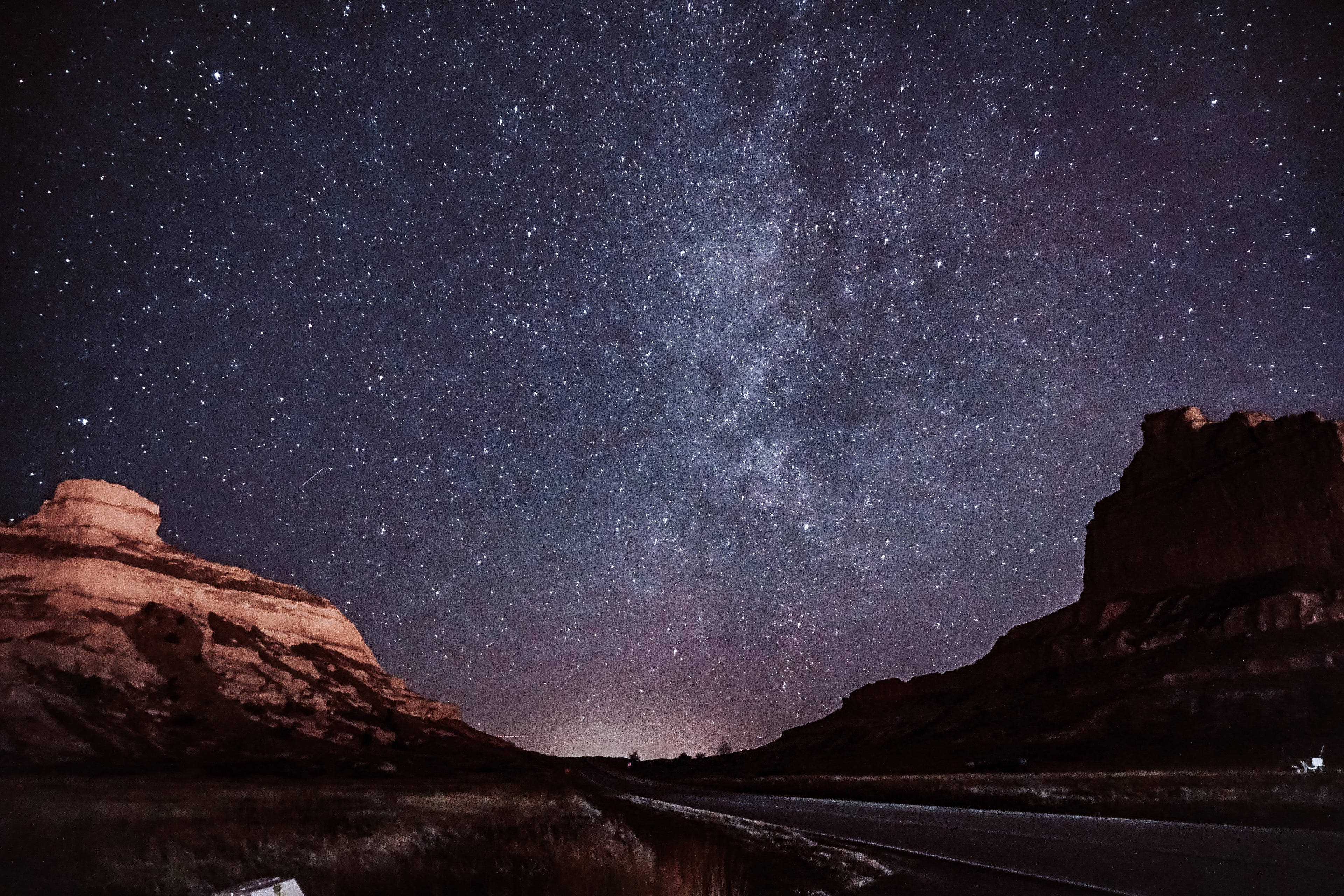 A view of the milky way galaxy above an open road through dessert canyons
